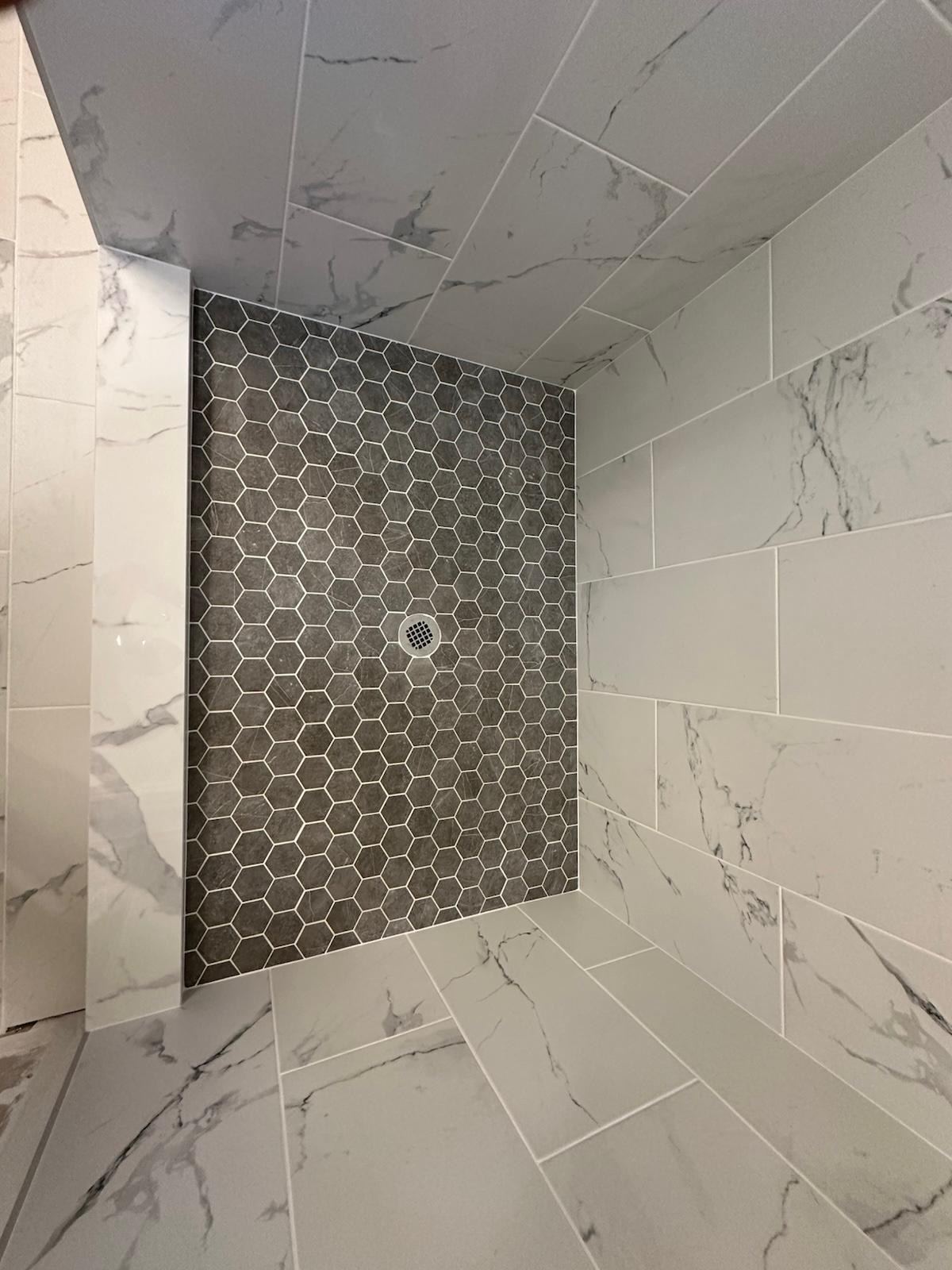 Charcoal hexagon mosaic shower floor accent against marble-look walls