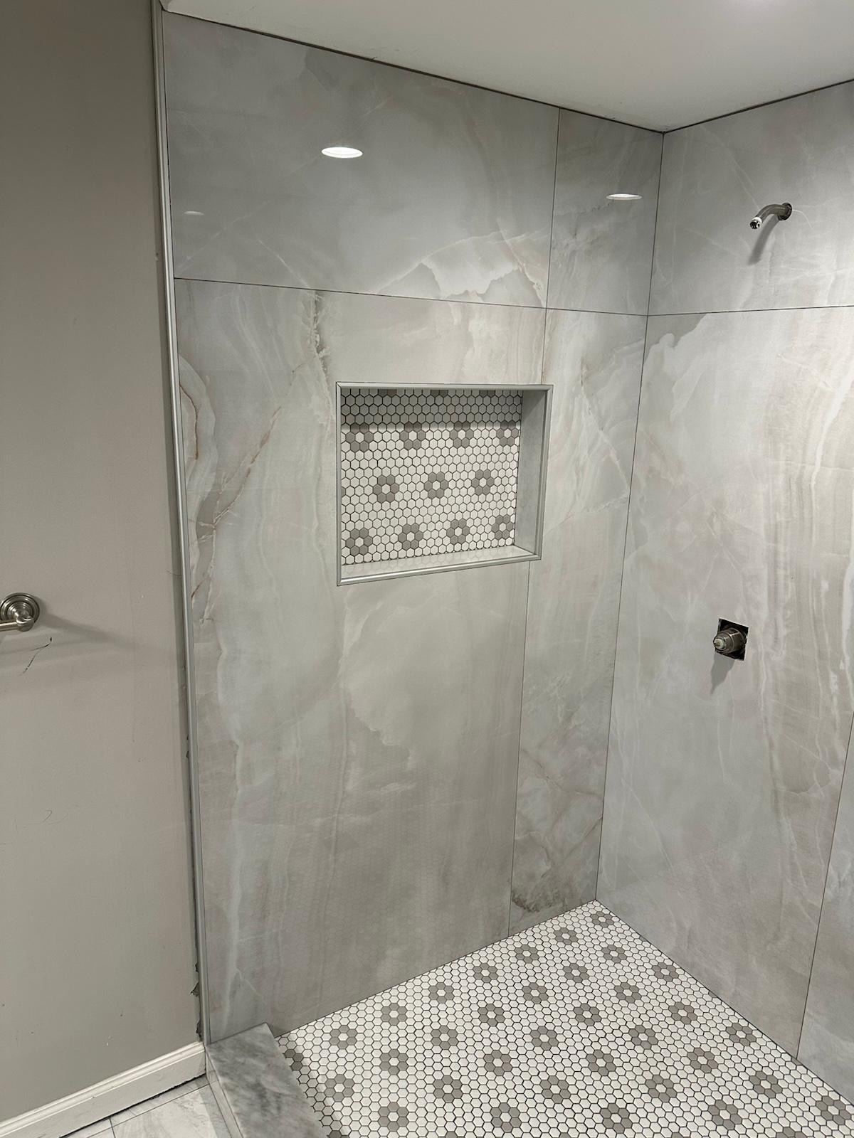 Built-in shower niche with mosaic tile lining inside a marble-look shower