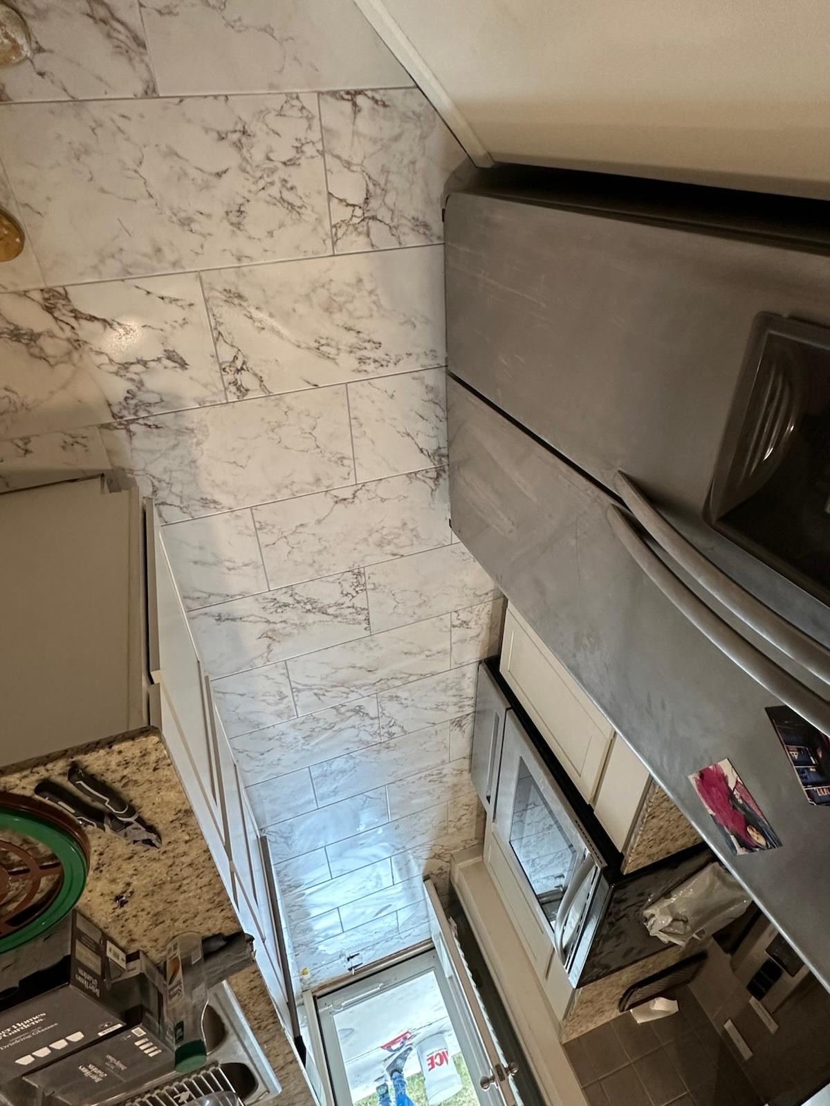 Marble-look tile wall installation in progress near a kitchen stairwell